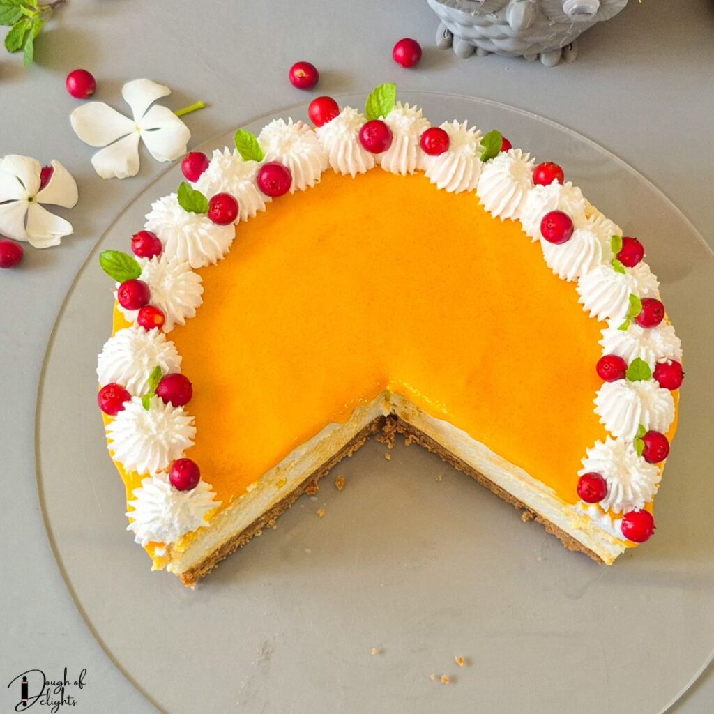 Creamy no-bake mango cheesecake decorated with whipped cream and fresh fruit