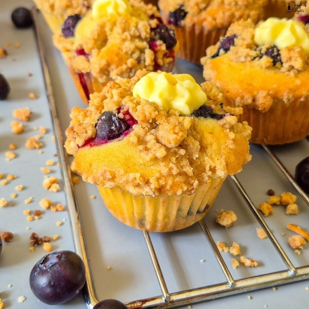 Close-up of a Blueberry Custard Crumble Muffin showing the soft crumb, juicy blueberries, crunchy crumble topping, and vanilla custard filling