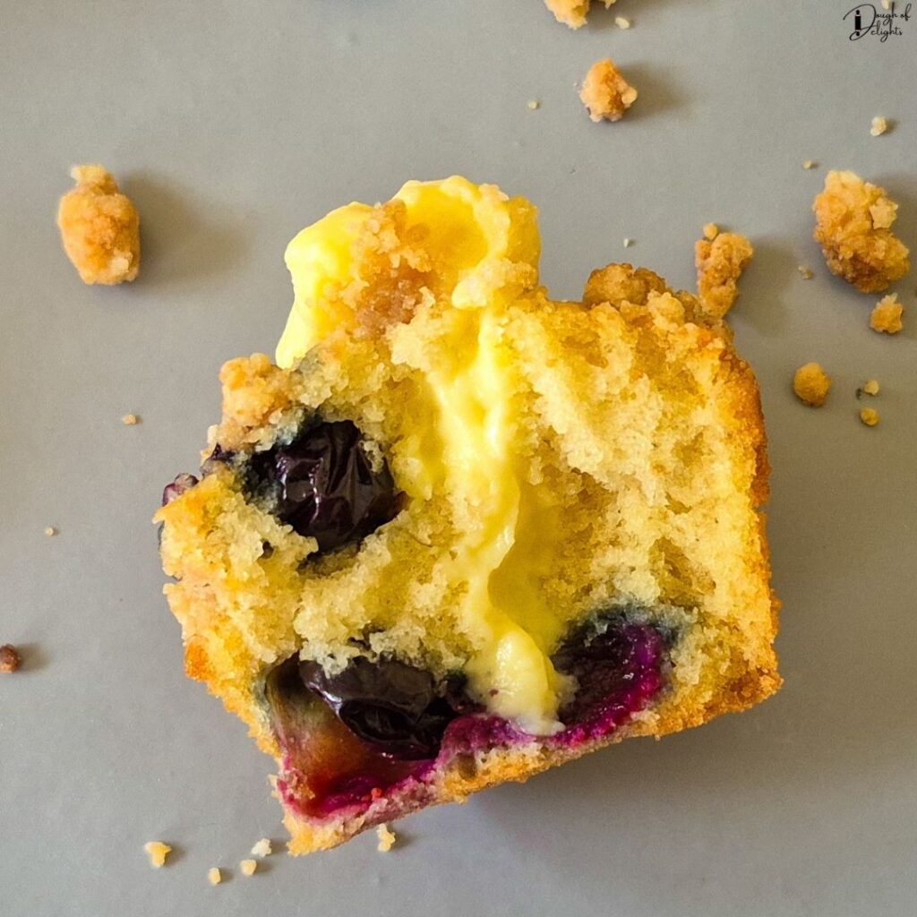A piece of Blueberry Custard Crumble Muffin broken in half to reveal the creamy vanilla custard filling inside