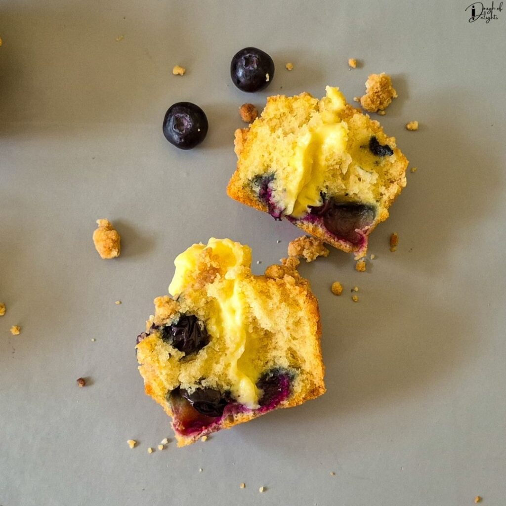 A Blueberry Custard Crumble Muffin broken in half to reveal the creamy vanilla custard filling inside
